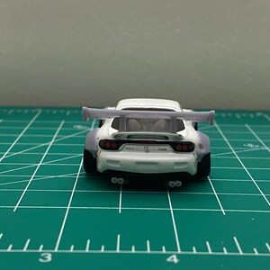 K&ouml;nnte beinhalten: Wei&szlig;es Diecast-Modellfahrzeug mit einem gro&szlig;en Heckfl&uuml;gel. Das Auto hat schwarze R&auml;der und rote R&uuml;ckleuchten. Das Auto steht auf einer gr&uuml;nen Schneidematte.
