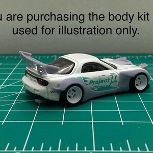 K&ouml;nnte beinhalten: Wei&szlig;es Modellauto mit gro&szlig;em Heckfl&uuml;gel, breiten Reifen und "Project &mu;" Schriftzug an der Seite. Das Auto steht auf einer gr&uuml;nen Schneidematte.