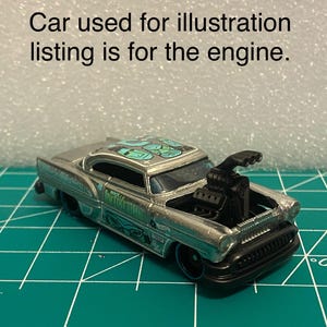 Peut inclure: Petite voiture argentée avec un moteur noir et des roues noires. La voiture présente un design détaillé avec le texte "TIKI TIME" sur le côté et un motif sur le toit. Le texte "Car used for illustration listing is for the engine" est au-dessus.