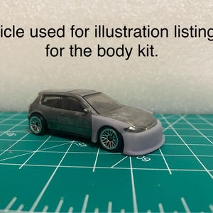 May include: A small-scale grey hatchback model car featuring a light grey custom front bumper and front fenders. The text 'Vehicle used for illustration listing is for the body kit.' is printed above the car. The car has silver wheels.