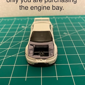 May include: A white toy car with the hood open, revealing the engine bay. The car is on a green cutting mat. Text at the top reads: "Car used for illustration only you are purchasing the engine bay."