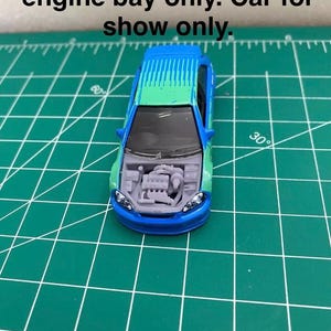 Puede incluir: Un coche de juguete azul y verde con un compartimento del motor detallado. El coche está sobre una estera de corte verde. El texto "You are purchasing the engine bay only. Car for show only." es visible sobre el coche.