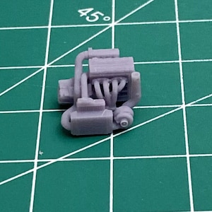 May include: A detailed model of a small, gray engine with a radiator and a set of pipes. The engine is made of plastic and is about 2 inches long.