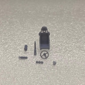 May include: A set of 1/24 scale model car interior parts, including a black racing seat, steering wheel, and other accessories.