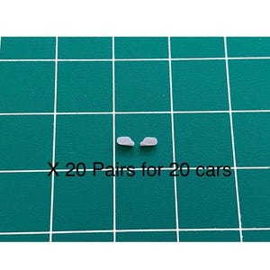 May include: Two small, light purple car parts are displayed on a green grid surface. The text "X 20 Pairs for 20 cars" is printed in white below the parts. The parts appear to be miniature car accessories.