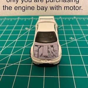 May include: A white toy car with the hood open, displaying a detailed engine bay. The image includes text: "Car used for illustration only you are purchasing the engine bay with motor."