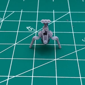 Könnte beinhalten: Ein graues Plastikmodell eines Automotors mit einem Vierzylinder-Ansaugkrümmer und Auspuffrohren.