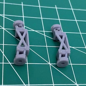 May include: Two gray plastic model airplane landing gear struts. The struts are made of a lightweight plastic and have a simple design.
