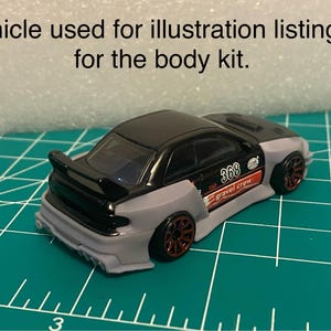 May include: A black and gray toy car with a spoiler and red wheels. The car has the number 368 and the words "gravel crew" on the side. The text at the top says "Vehicle used for illustration listing is for the body kit."