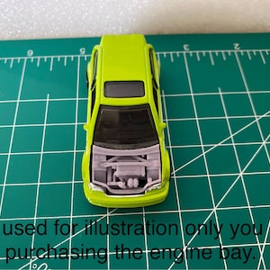 May include: A lime green toy car with the hood open, revealing a detailed engine bay. The car sits on a green cutting mat with inch measurements. Text at the bottom reads: "Car used for illustration only you are purchasing the engine bay."