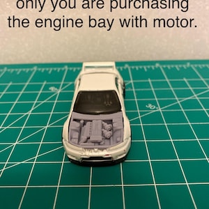 May include: A white toy car with the hood open, revealing the engine bay and motor. The text at the top of the image reads, "Car used for illustration only you are purchasing the engine bay with motor."