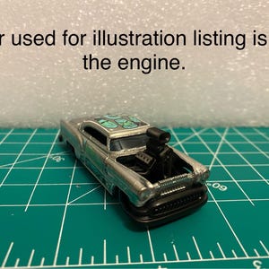 Pode incluir: Carro de brinquedo prateado com motor preto e teto com padrão verde e prateado. O capô está aberto, revelando o motor. O carro está sobre uma superfície de grade verde. O texto na imagem diz: "Carro usado para listagem de ilustração é para o motor."