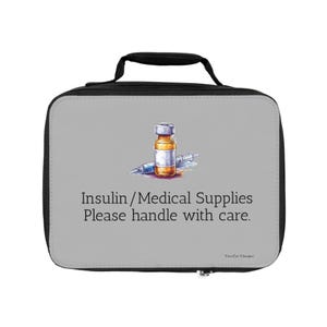 Op de afbeelding: Een grijze lunchtas met een zwarte rits en handvat. De tas heeft een tekening van een insulineflesje en een spuit met de tekst "Insulin/Medical Supplies Please handle with care."