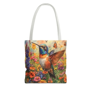 May include: A colorful tote bag featuring a hummingbird in flight with its wings spread wide. The hummingbird is surrounded by a variety of flowers in shades of pink, purple, yellow, and orange. The background is a soft, pastel blue.