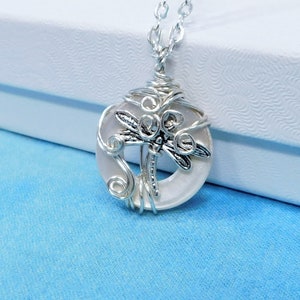 May include: A silver chain necklace with a white round pendant featuring a silver dragonfly design.