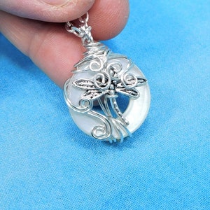 May include: A silver wire wrapped pendant featuring a white iridescent shell with a silver dragonfly design.