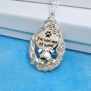 May include: Silver necklace with a wire-wrapped pendant featuring a dog silhouette and the text "You had me at woof".