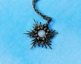 May include: A necklace featuring a star-shaped pendant crafted from dark bronze-toned wire wrapped around a central pale, translucent round stone. The pendant is attached to a matching dark bronze-toned metal chain with small circular links.
