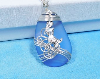 May include: A silver chain necklace with a blue glass pendant featuring a mermaid design wrapped in silver wire.