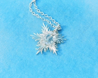 May include: A silver-toned necklace featuring a star-shaped pendant crafted from thin, radiating wire strands. The center of the star is accented with a clear, faceted crystal bead. The pendant hangs from a delicate, matching silver-toned link chain.