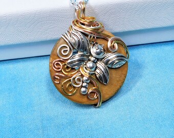 May include: A round wooden pendant necklace featuring a silver-toned dragonfly charm centered on the wood. The pendant is wrapped in decorative silver, copper, and gold-colored wire swirls and hangs from a simple silver-toned metal chain.