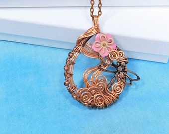 Puede incluir: Collar de alambre de cobre con un diseño de libélula y flor. El colgante tiene forma de lágrima y presenta una flor rosa con un centro amarillo.
