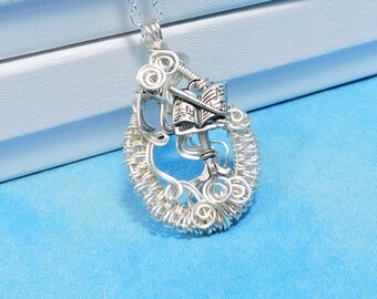 May include: A silver-toned wire-wrapped pendant necklace featuring a central charm shaped like an open book with visible musical notes on the pages. The pendant is constructed from intricate coiled silver wire forming an oval frame around the book.