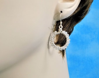 May include: A silver-toned earring featuring a circular hoop design adorned with a series of small, clear, faceted beads arranged around the entire perimeter. The earring hangs from a simple silver-toned hook wire, creating a dangling effect.