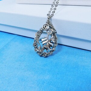 May include: A silver wire wrapped pendant necklace featuring a dragon design. The pendant is oval shaped and hangs from a silver chain.