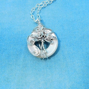 May include: A silver chain necklace with a white shell pendant featuring a silver dragonfly wire wrapped design.