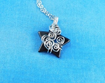 May include: A silver chain necklace with a black star pendant. The star is wrapped with silver wire in a decorative swirl pattern. The background is a solid blue.