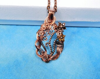 May include: A copper-toned wire-wrapped pendant necklace featuring intricate swirling metal patterns, a small leaf accent, and two floral motifs adorned with small amber-colored crystals, suspended from a matching copper-toned metal chain.