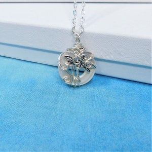 May include: A silver necklace with a white iridescent pendant featuring a dragonfly design. The pendant is made of wire wrapped around a round piece of glass.