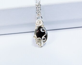 May include: A silver-toned wire-wrapped pendant necklace featuring a smooth, dark brown oval gemstone. The metal wire is coiled into intricate loops around the stone, and the pendant hangs from a matching silver-toned link chain necklace.