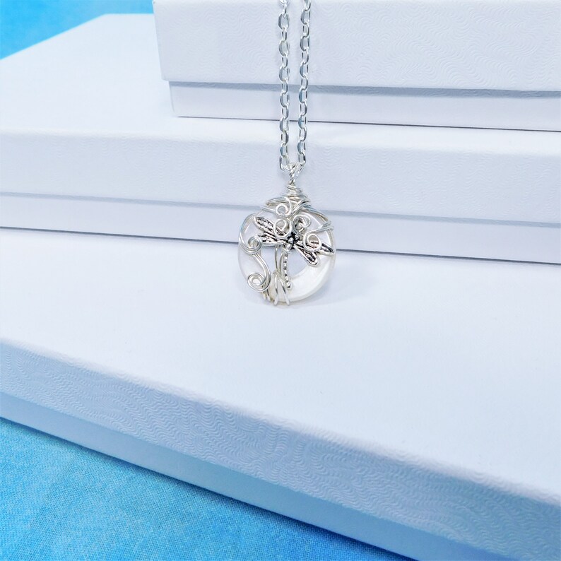 May include: A silver chain necklace with a white, round pendant featuring a silver dragonfly design.