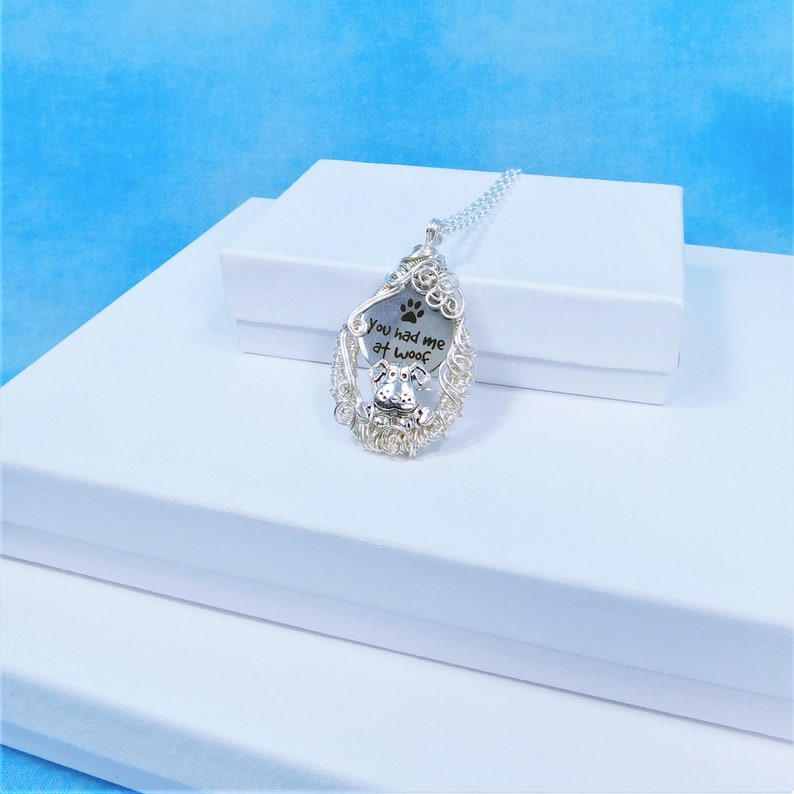 May include: Silver necklace with a pendant featuring a dog silhouette and the inscription "You had me at woof" with a paw print.