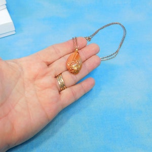 May include: A gold wire wrapped pendant with a teardrop shaped agate stone. The stone is a mix of orange, brown, and white colors. The pendant is hanging from a silver chain.