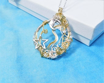 Puede incluir: Un collar con un colgante de alambre envuelto en plata y oro que presenta una luna creciente, una estrella y remolinos. El colgante cuelga de una cadena de plata.