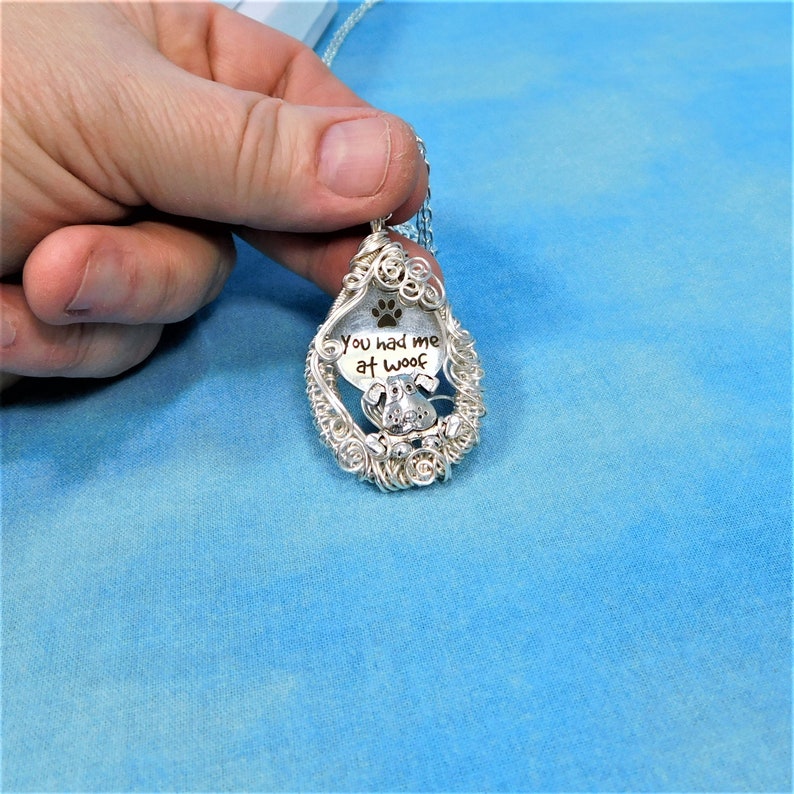 May include: Silver wire wrapped pendant necklace with a dog paw print and the text "You had me at woof".