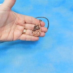 May include: A copper wire wrapped pendant necklace with a teardrop shape. The pendant features a swirl design with a copper colored stone in the center.