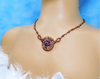 May include: A necklace featuring a central circular pendant crafted from intricate copper wire wrapping, which secures a single round purple gemstone. The chain is composed of small copper beads and wire-wrapped links, creating a cohesive metallic design.