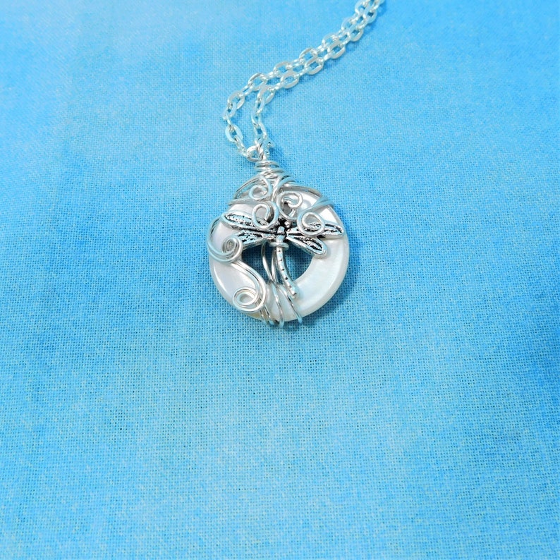 May include: A silver chain necklace with a white shell pendant featuring a silver dragonfly wire wrapped design.