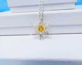 May include: A silver-toned wire-wrapped pendant necklace featuring a central amber-colored spherical bead surrounded by radiating silver wire spikes. The pendant hangs from a matching silver-toned chain, creating a starburst or floral appearance.