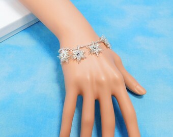 May include: A silver-toned chain bracelet featuring multiple star-shaped charms with pointed rays and small clear beads at the center of each star. The bracelet is secured with a metal clasp and displays a metallic finish throughout the design.