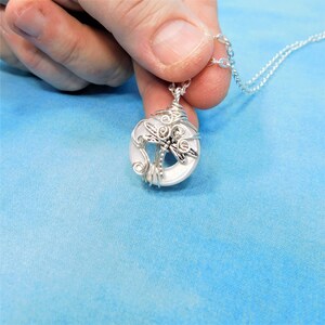 May include: A silver necklace with a white pendant featuring a dragonfly design. The pendant is made of wire wrapped around a round, white stone.