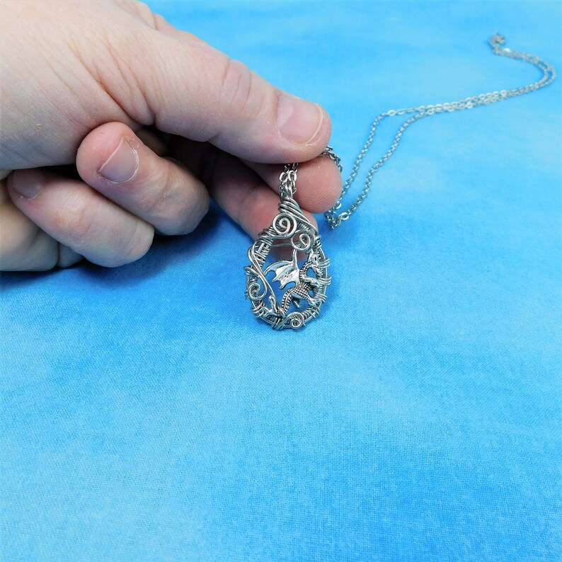 May include: A silver wire-wrapped pendant featuring a dragon design. The pendant is attached to a silver chain.