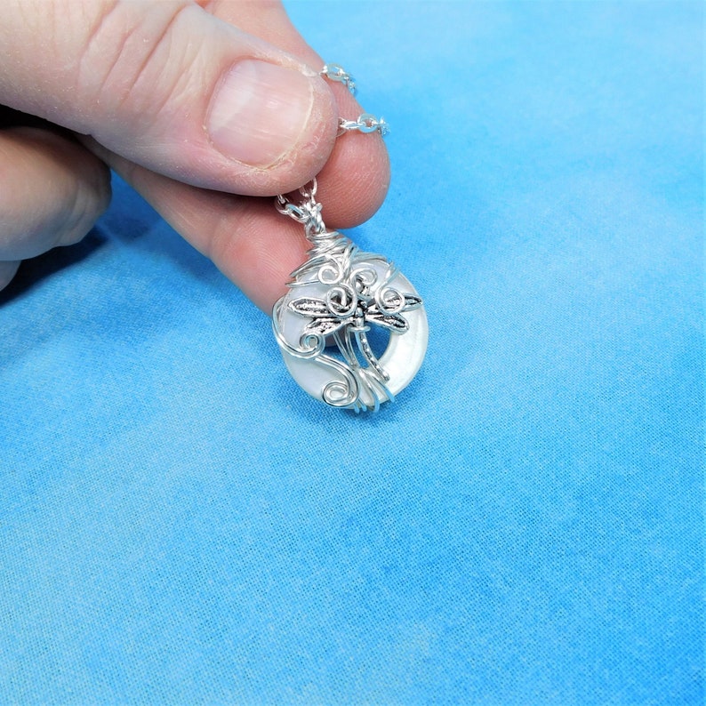 May include: A silver wire wrapped pendant featuring a white iridescent shell with a silver dragonfly design.
