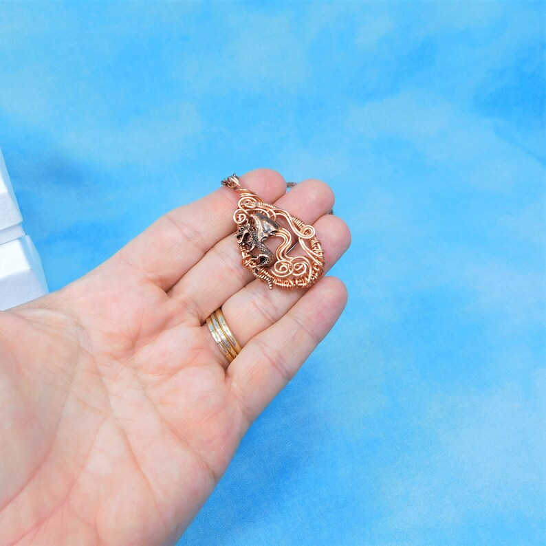 May include: A copper wire pendant necklace with a swirling design and a brown stone in the center.