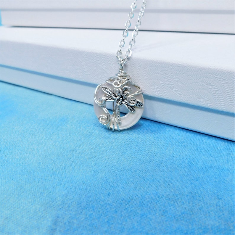 May include: A silver chain necklace with a white round pendant featuring a silver dragonfly design.