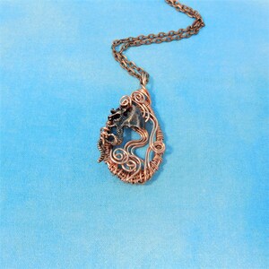 May include: A copper wire wrapped pendant necklace featuring a small dragon figurine. The pendant is shaped like a teardrop and has a swirling wire design.